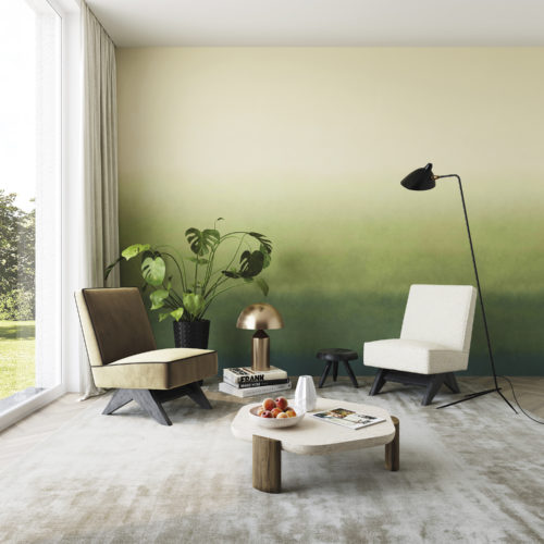 Un salon impressionnant avec deux canapés à une place, une table basse en bois de forme géométrique, un lampadaire noir minimal et une grande fenêtre pour apporter de la luminosité à l'espace. Nous voyons un mur d'accent recouvert du motif "Zenitude" de la collection Joy d'Omexco : un dégradé de nuances de vert d'une beauté à couper le souffle.